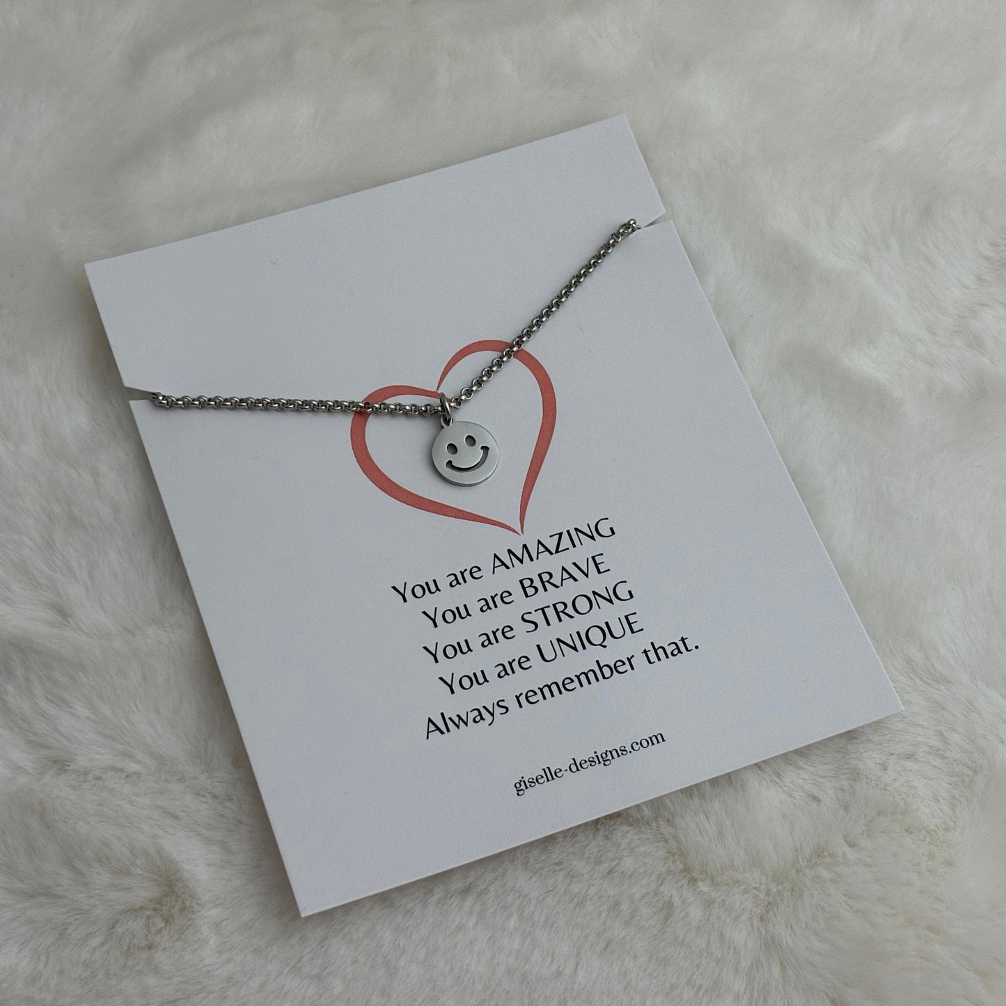 Necklace with a heart-shaped pendant on a card with motivational text, placed on a soft white surface.