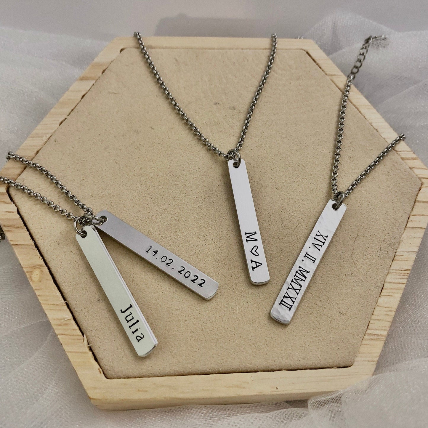 Three silver necklaces with engraved names on a wooden display box.