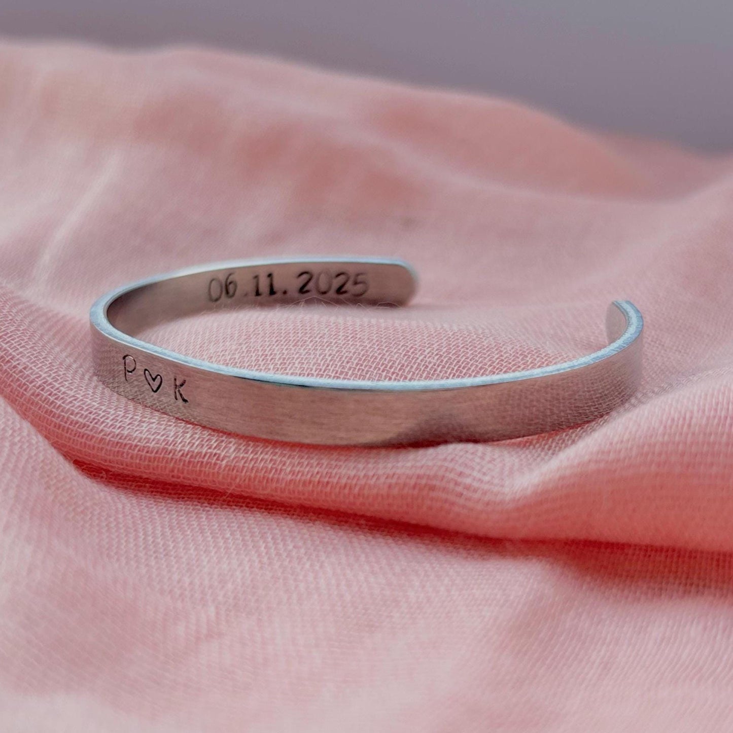 Silver bracelet with engraved text on a pink fabric background