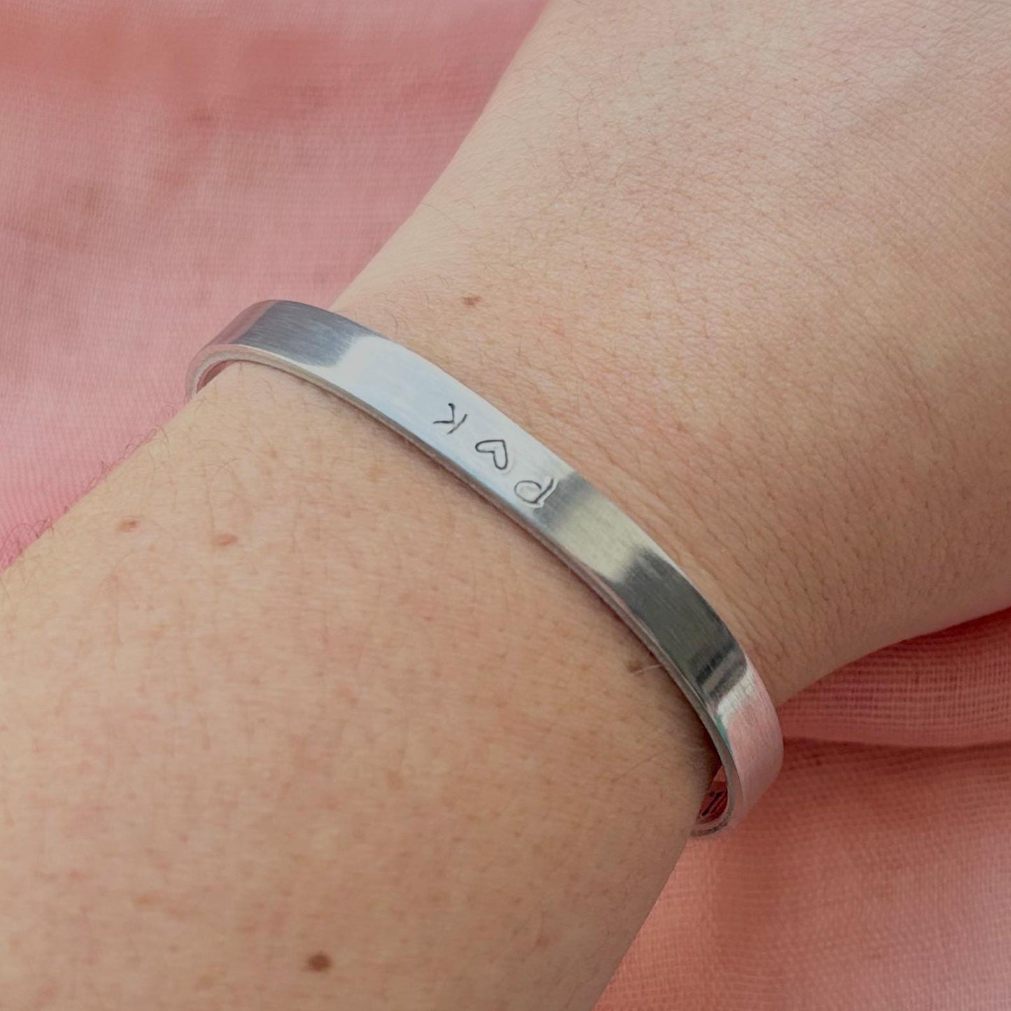 Silver bracelet on a wrist with a pink fabric background