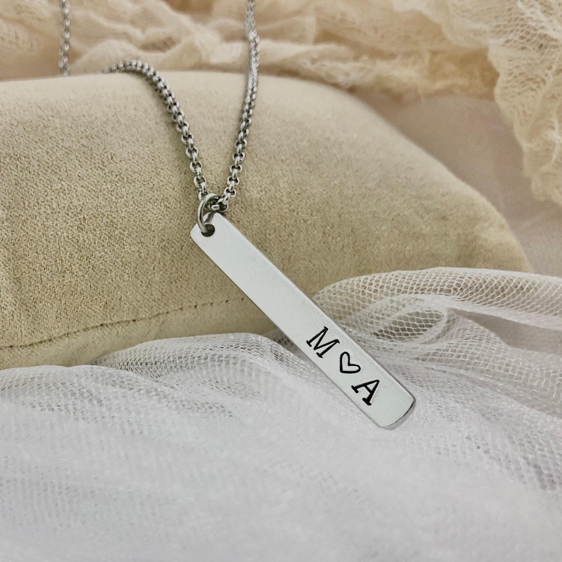 Silver necklace with a bar pendant featuring 'M A' on a soft fabric background