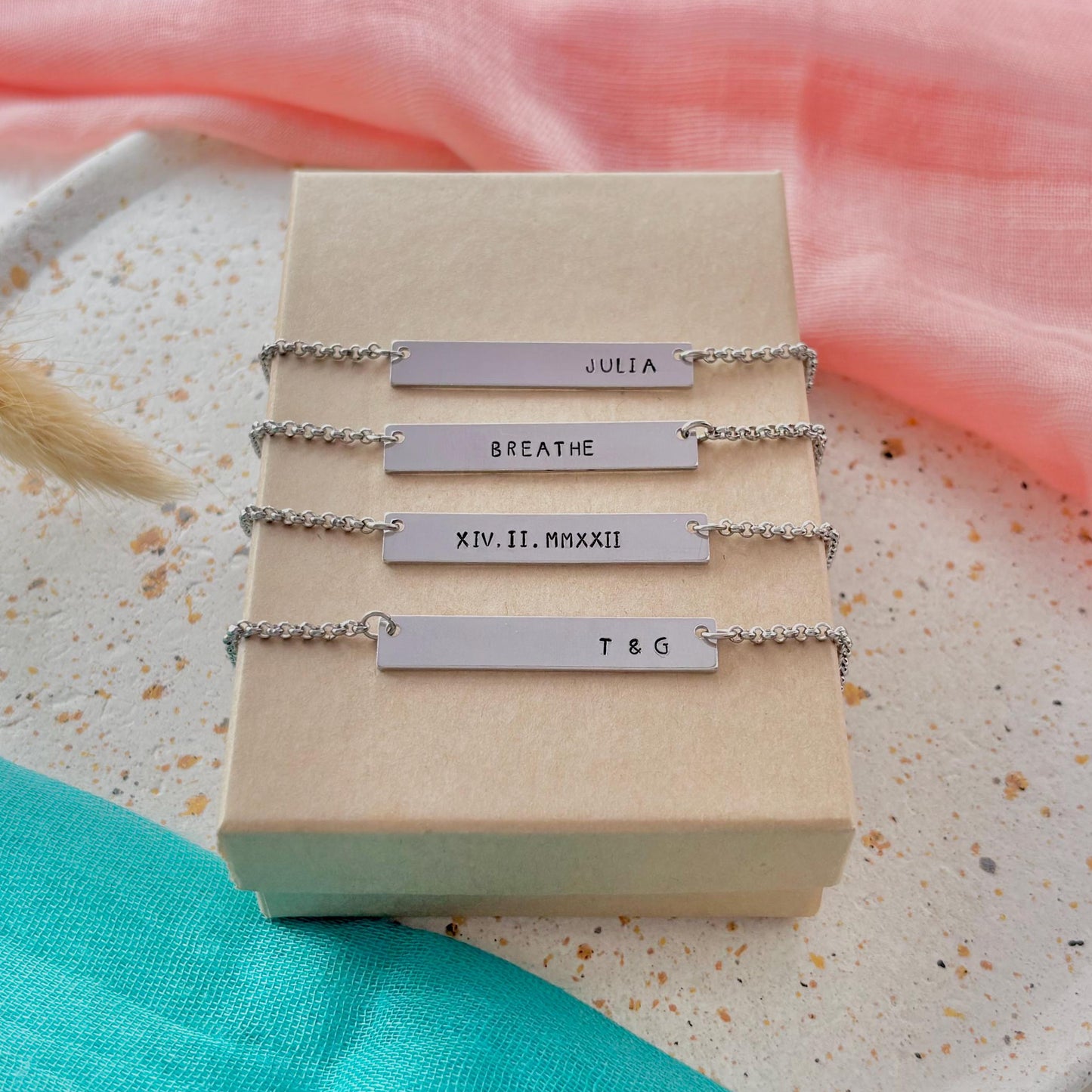 Set of silver bar necklaces on a display card with a pink and green fabric background