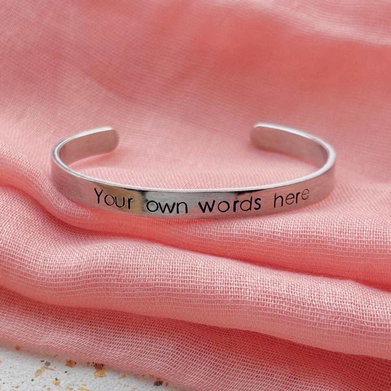 Silver bracelet with 'Your own words here' engraving on pink fabric