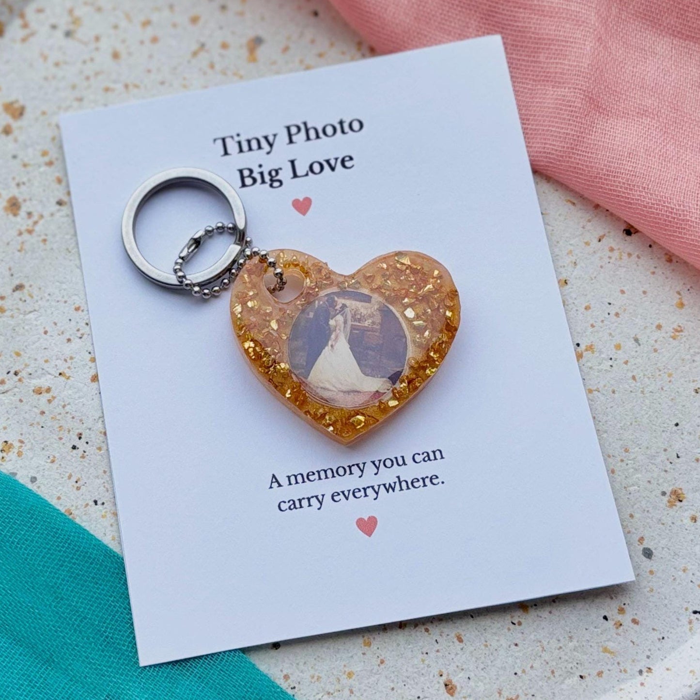 Heart-shaped keychain with a photo on a card with text, placed on a speckled plate.