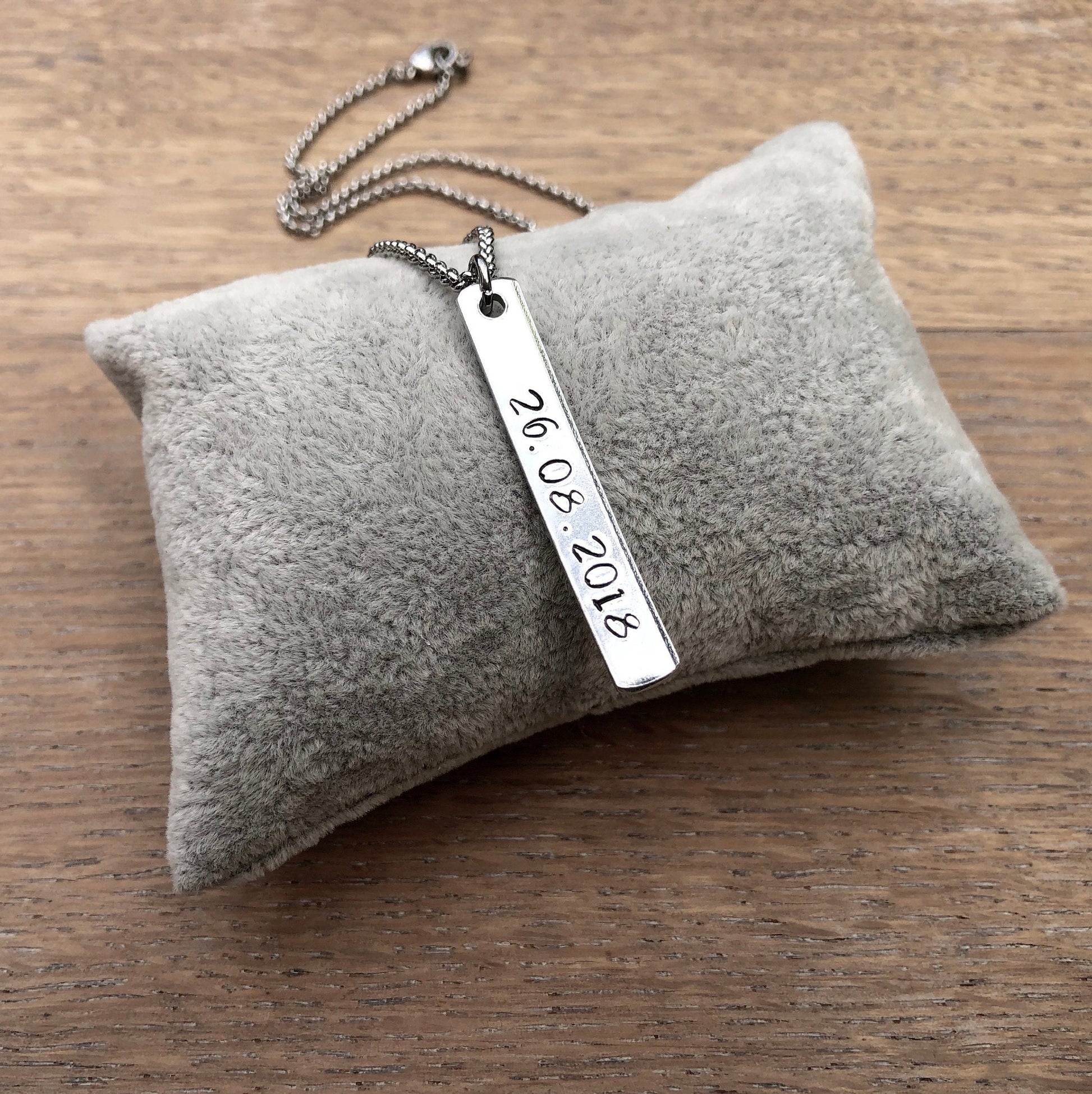 Silver necklace with a bar pendant on a gray cushion against a wooden background