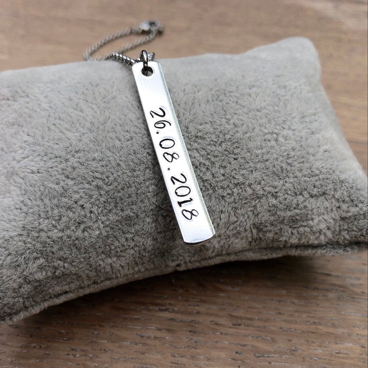 Silver necklace with a engraved date tag on a gray cushion