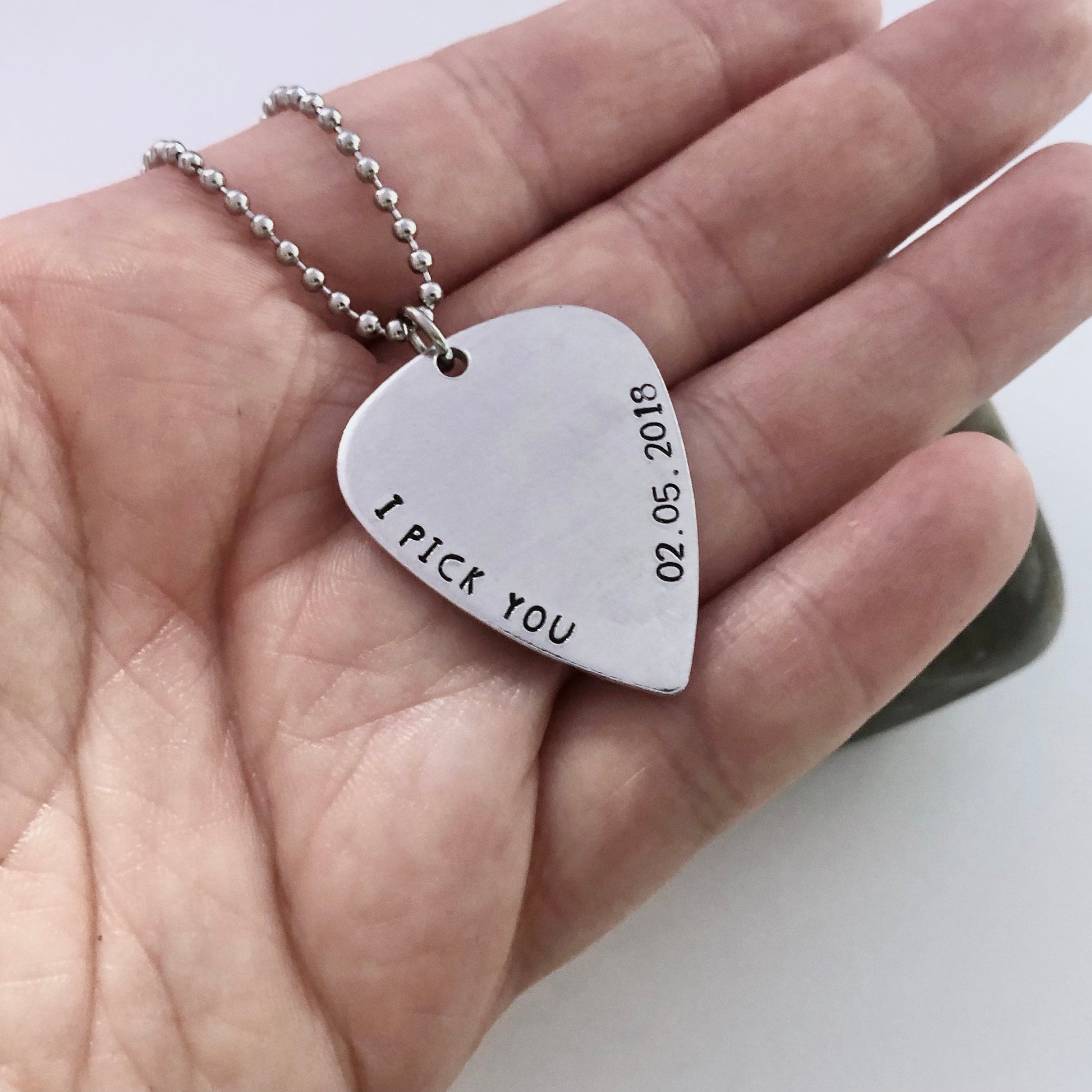 Guitar pick shaped pendant with 'I pick you' engraving on a hand
