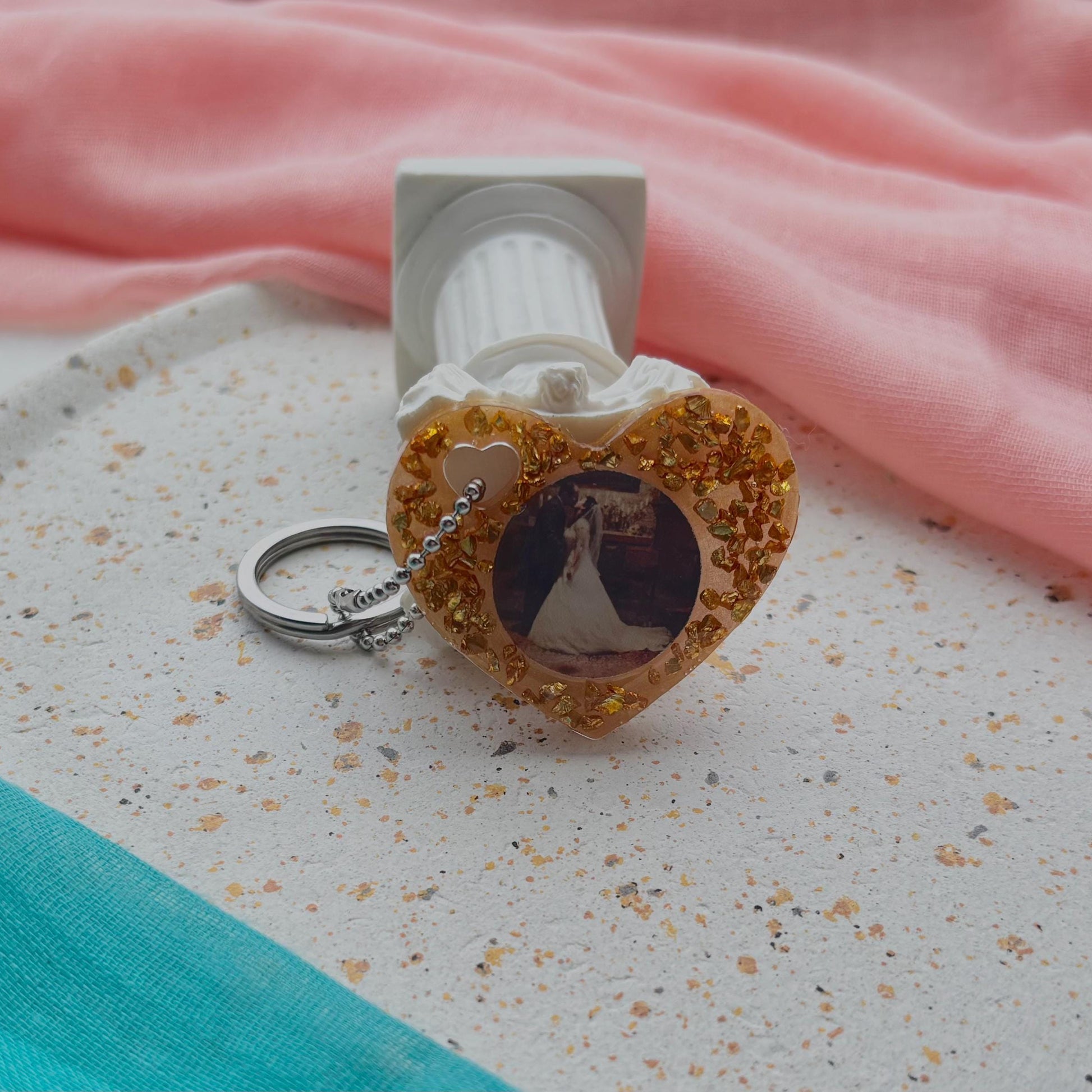 Heart-shaped keychain with a photo of a sailboat on a textured surface with pink fabric in the background