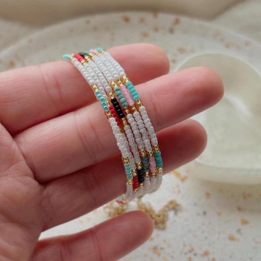 Hand holding a stack of colorful beaded bracelets on a neutral background