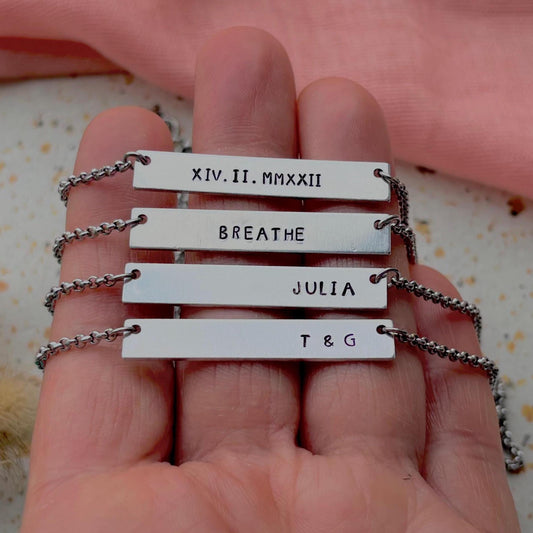 Hand holding a necklace with engraved nameplates.