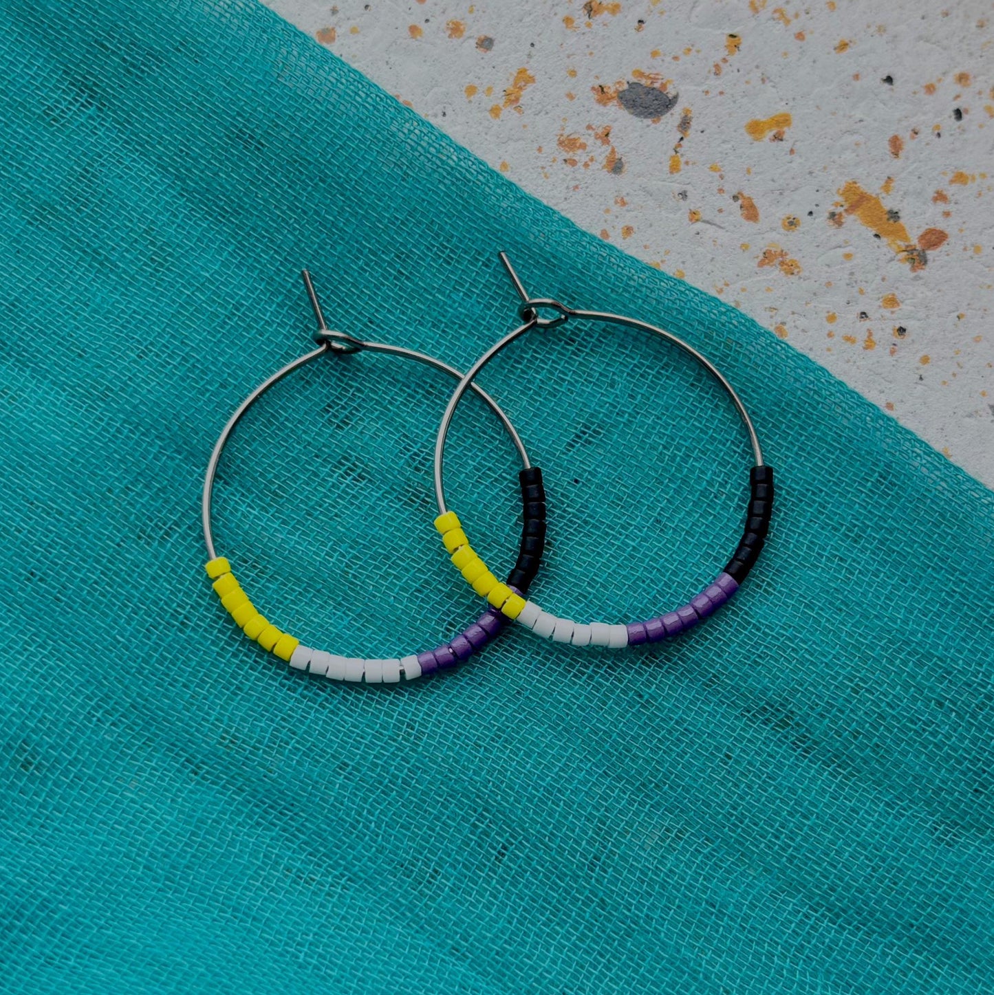Hoop earrings with colorful beads on a turquoise fabric background