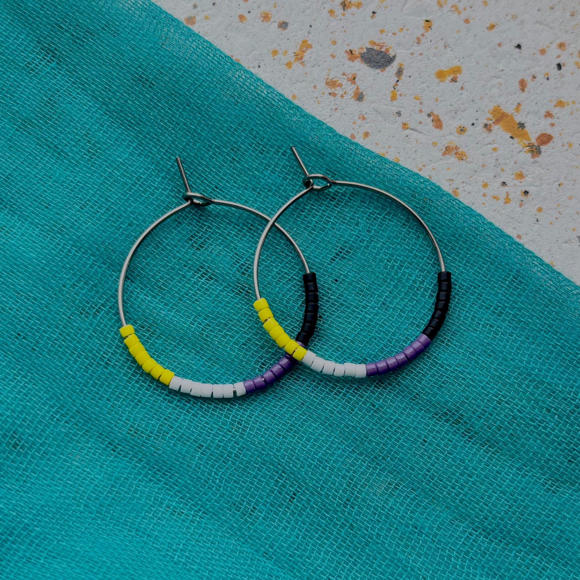 Hoop earrings with colorful beads on a turquoise fabric background