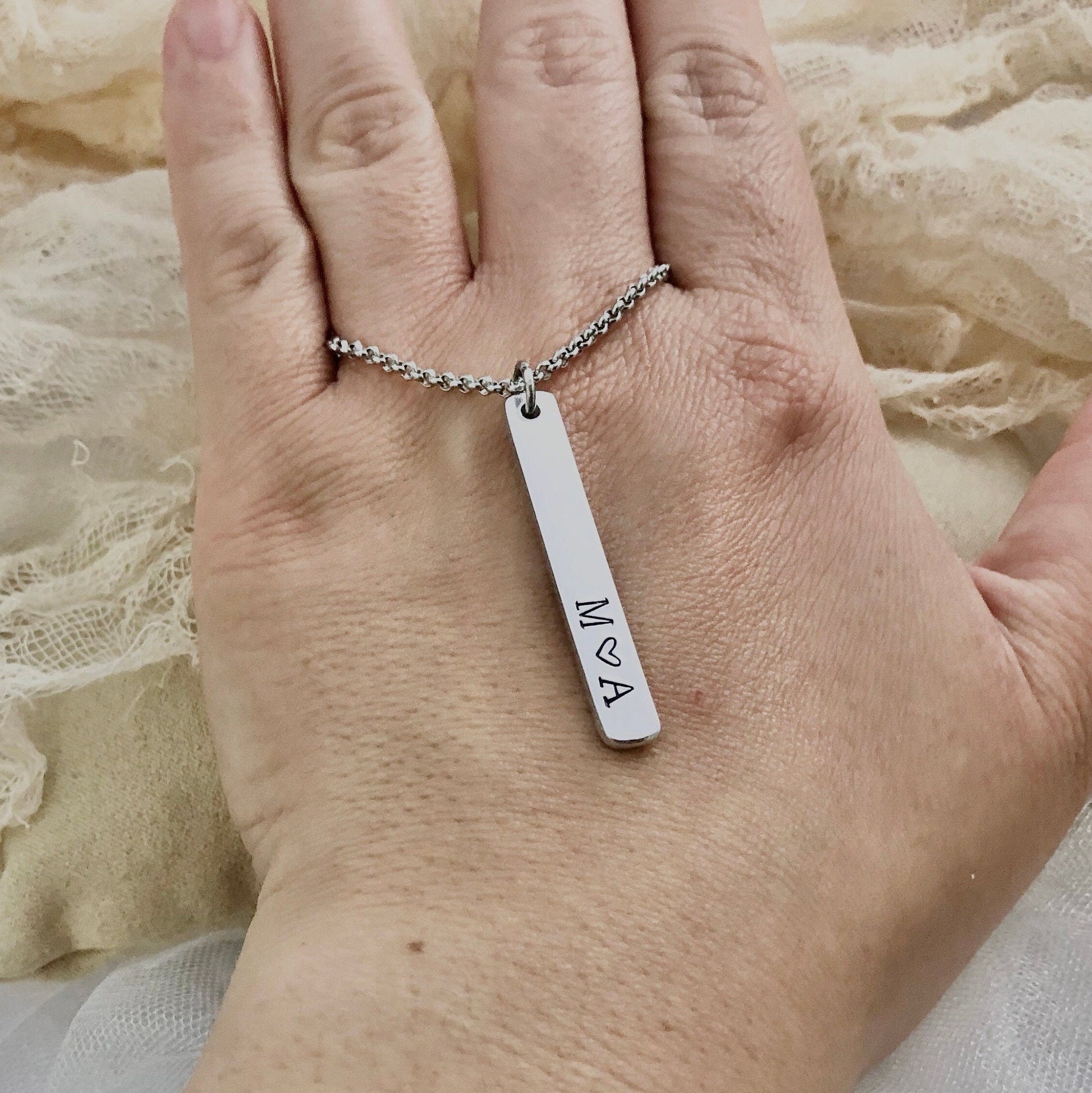 Hand wearing a silver necklace with a bar pendant on a textured fabric background