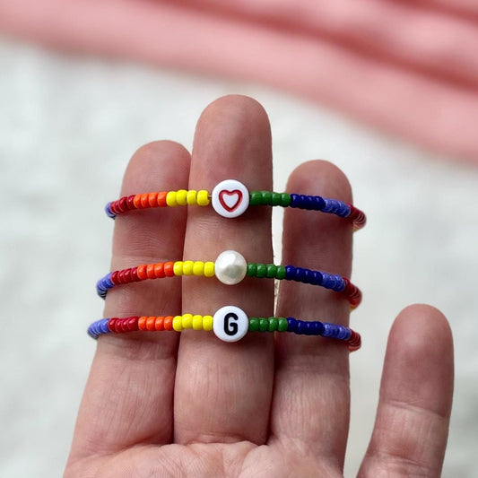 Colorful beaded bracelets with letter and heart charms on a hand against a blurred background