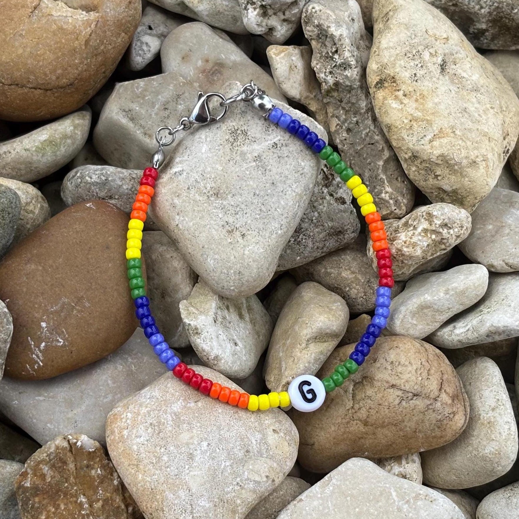 Colorful beaded bracelet with a letter 'G' charm on pebbles