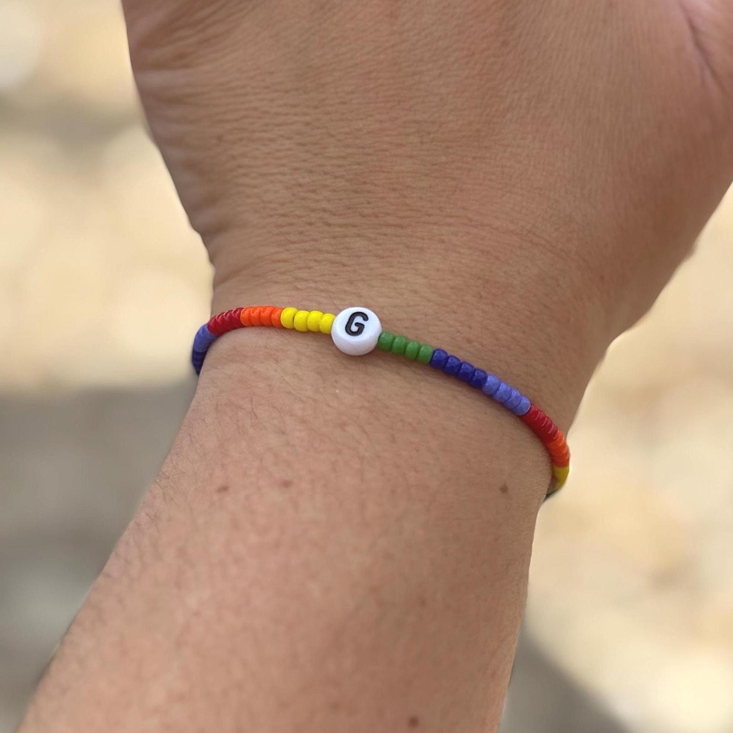 Colorful beaded bracelet with a letter 'G' on a wrist against a blurred natural background