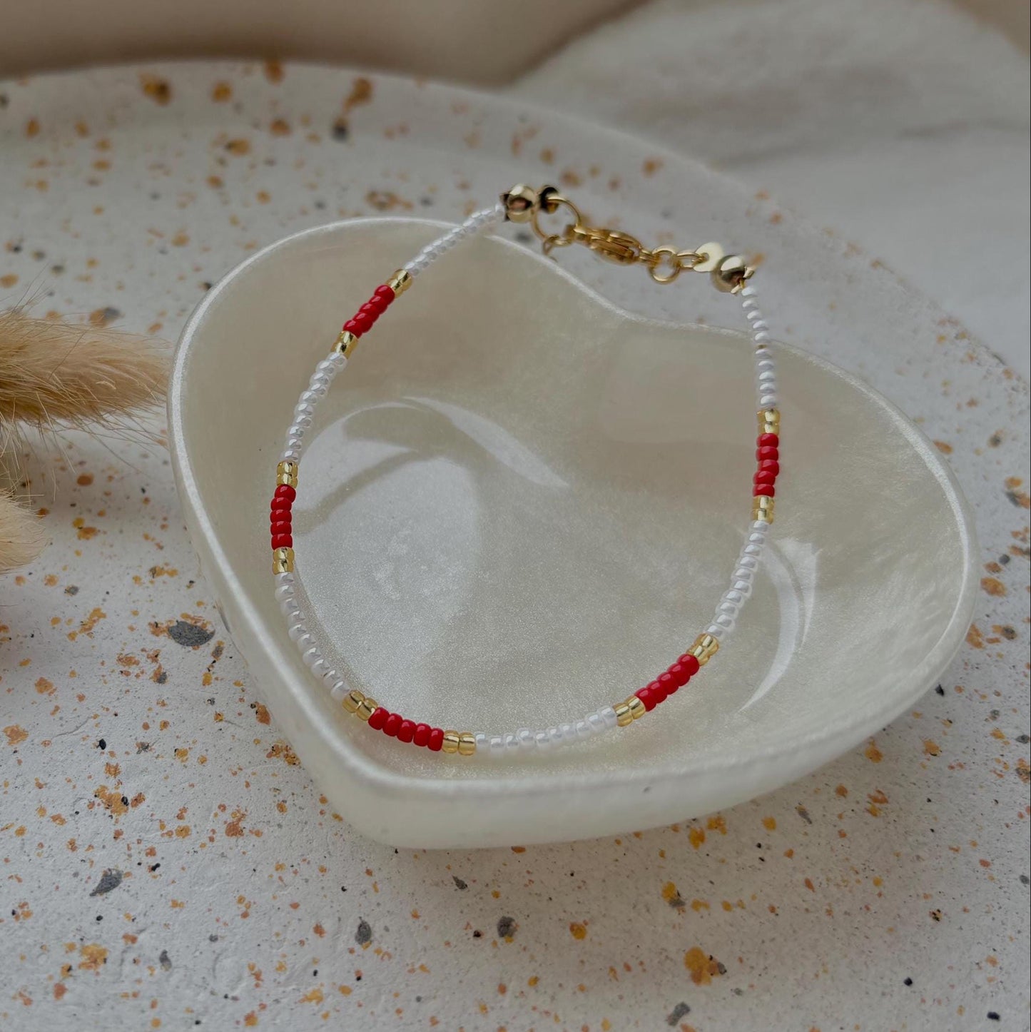 Bracelet with red and gold accents on a white dish with a textured surface