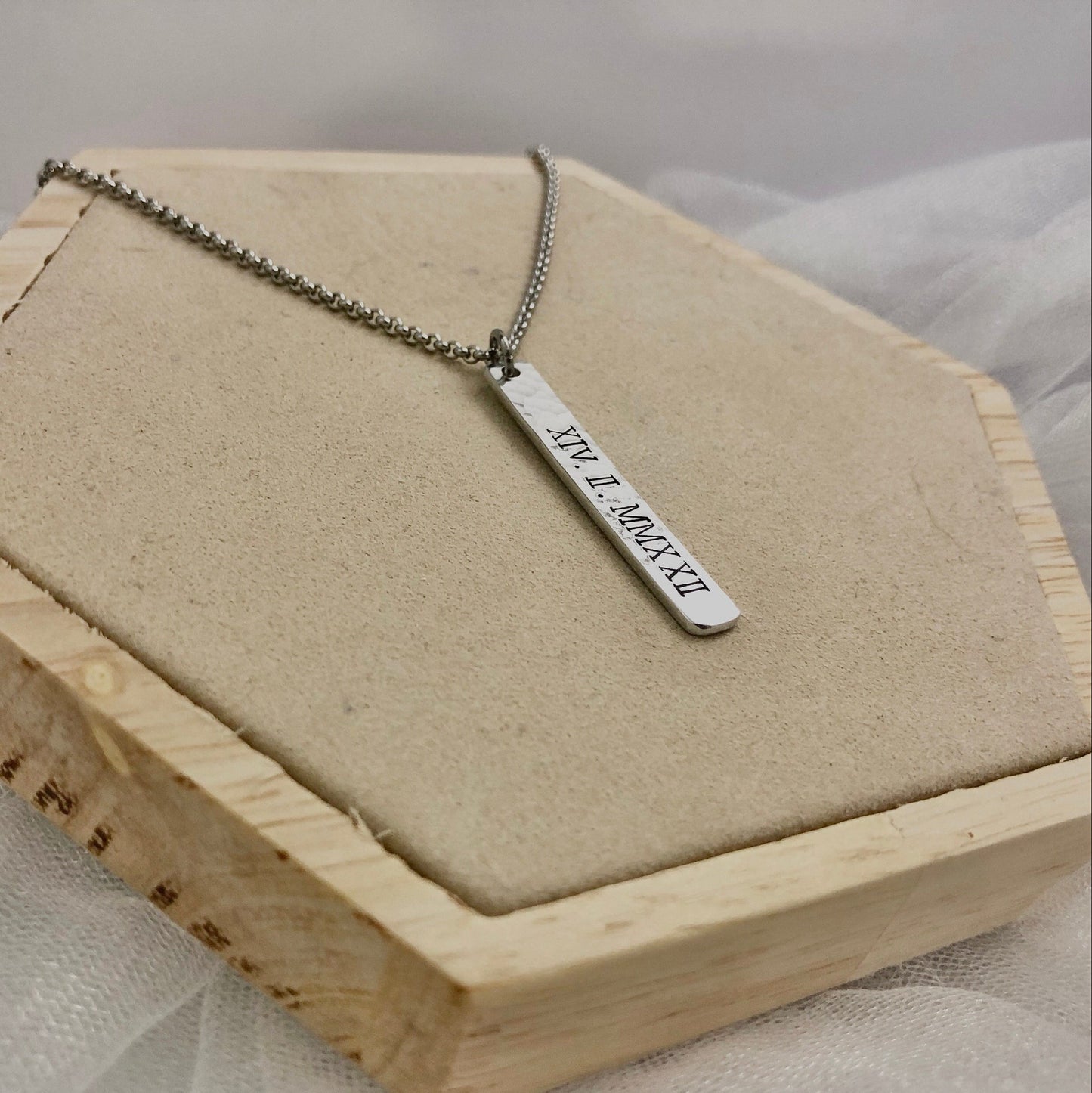 Silver necklace with a bar pendant on a wooden stand