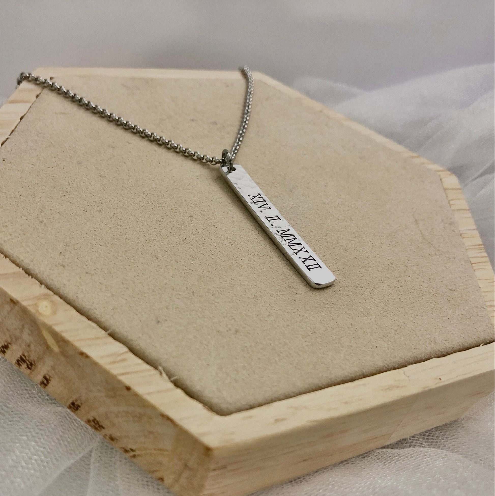 Silver necklace with a bar pendant on a wooden stand