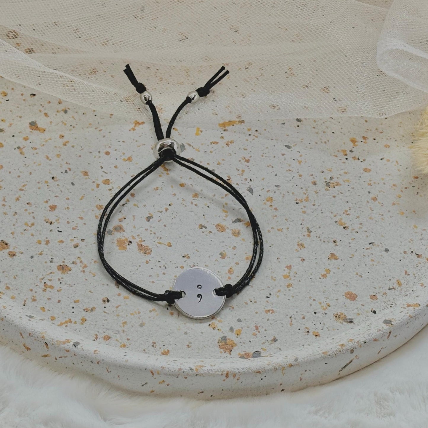 Black cord bracelet with a silver button charm on a textured surface