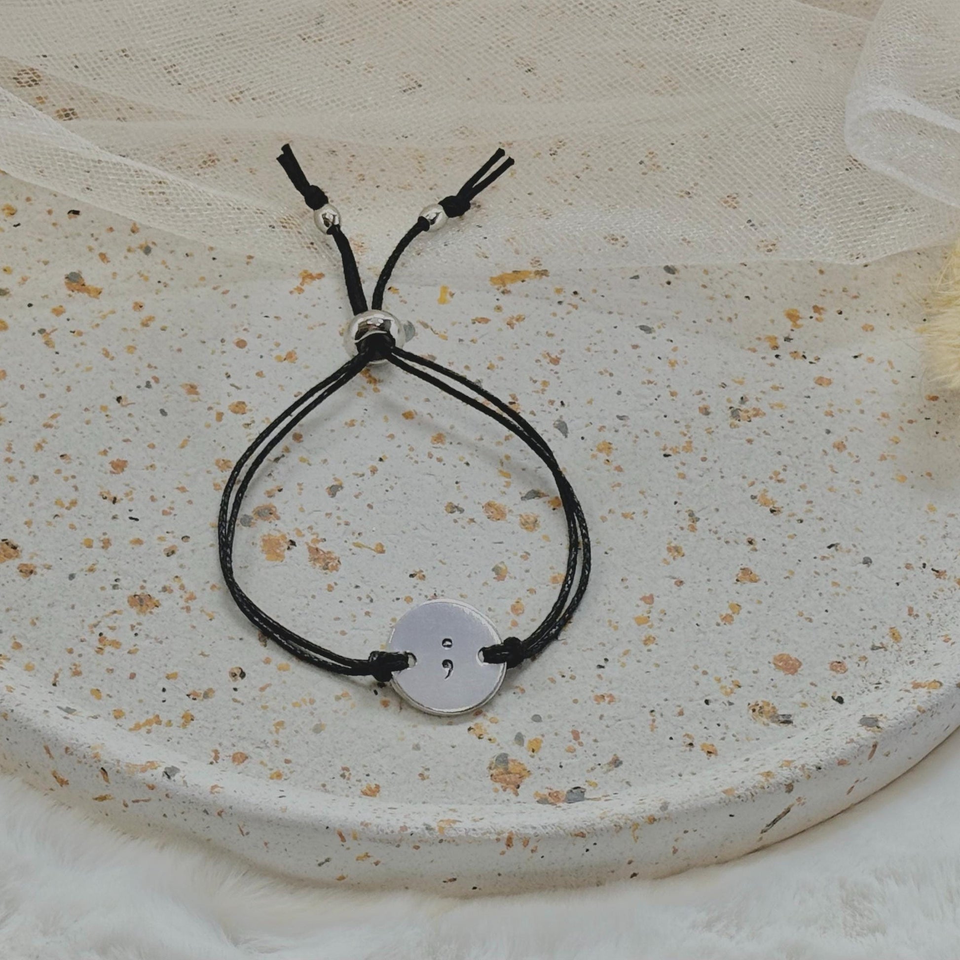 Black cord bracelet with a silver button charm on a textured surface