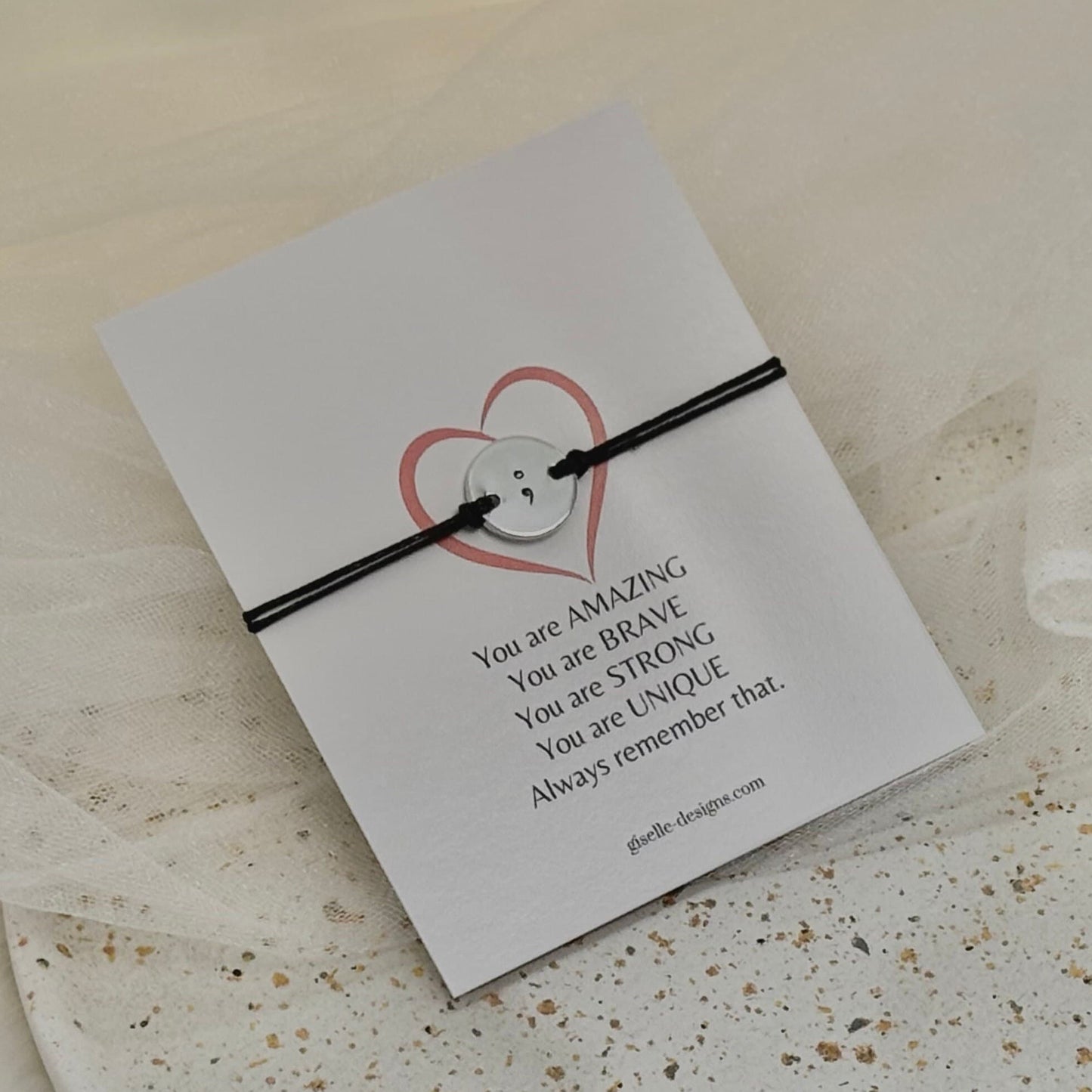 Black cord bracelet on a card with motivational message on a textured surface