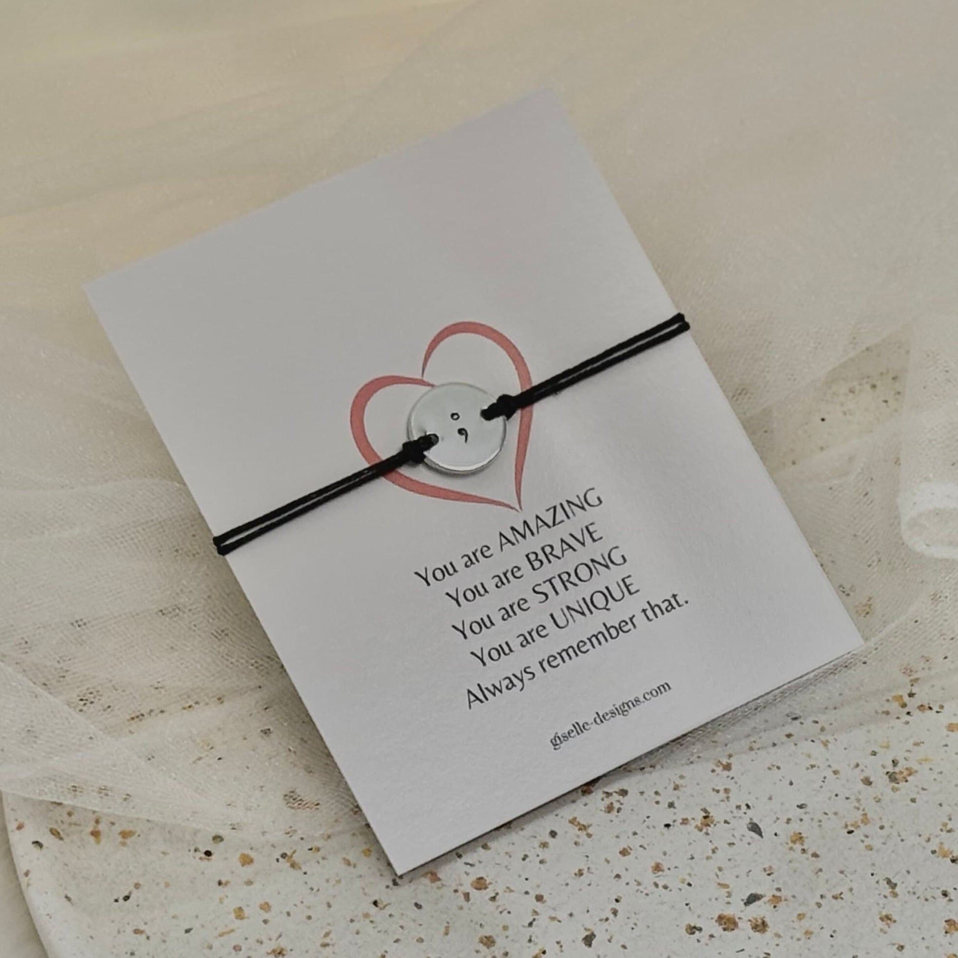 Black cord bracelet on a card with motivational message on a textured surface