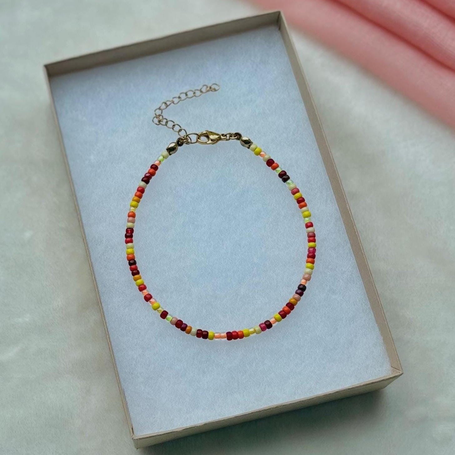 Beaded anklet on a white box with a pink fabric background