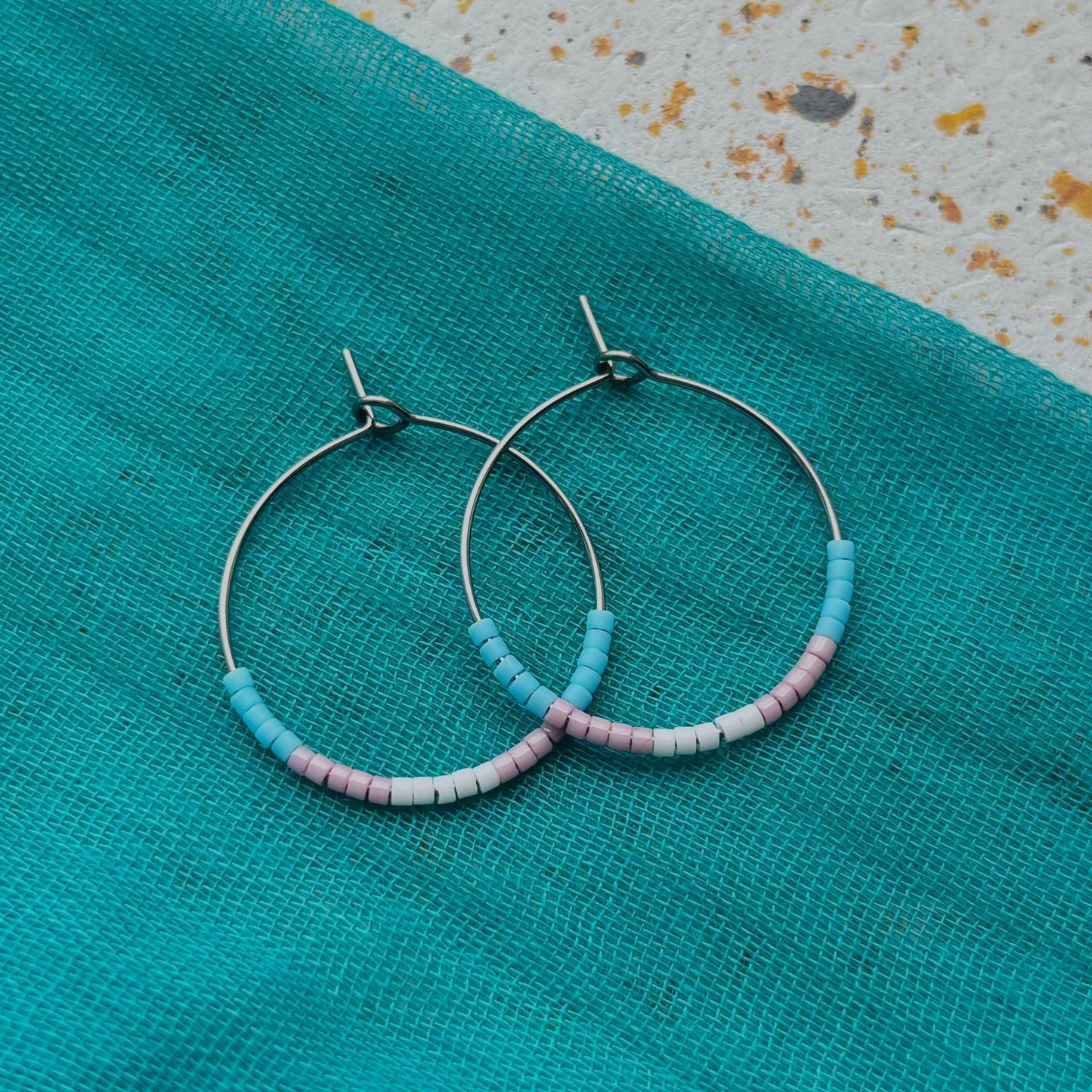 Hoop earrings with beaded accents on a turquoise fabric background