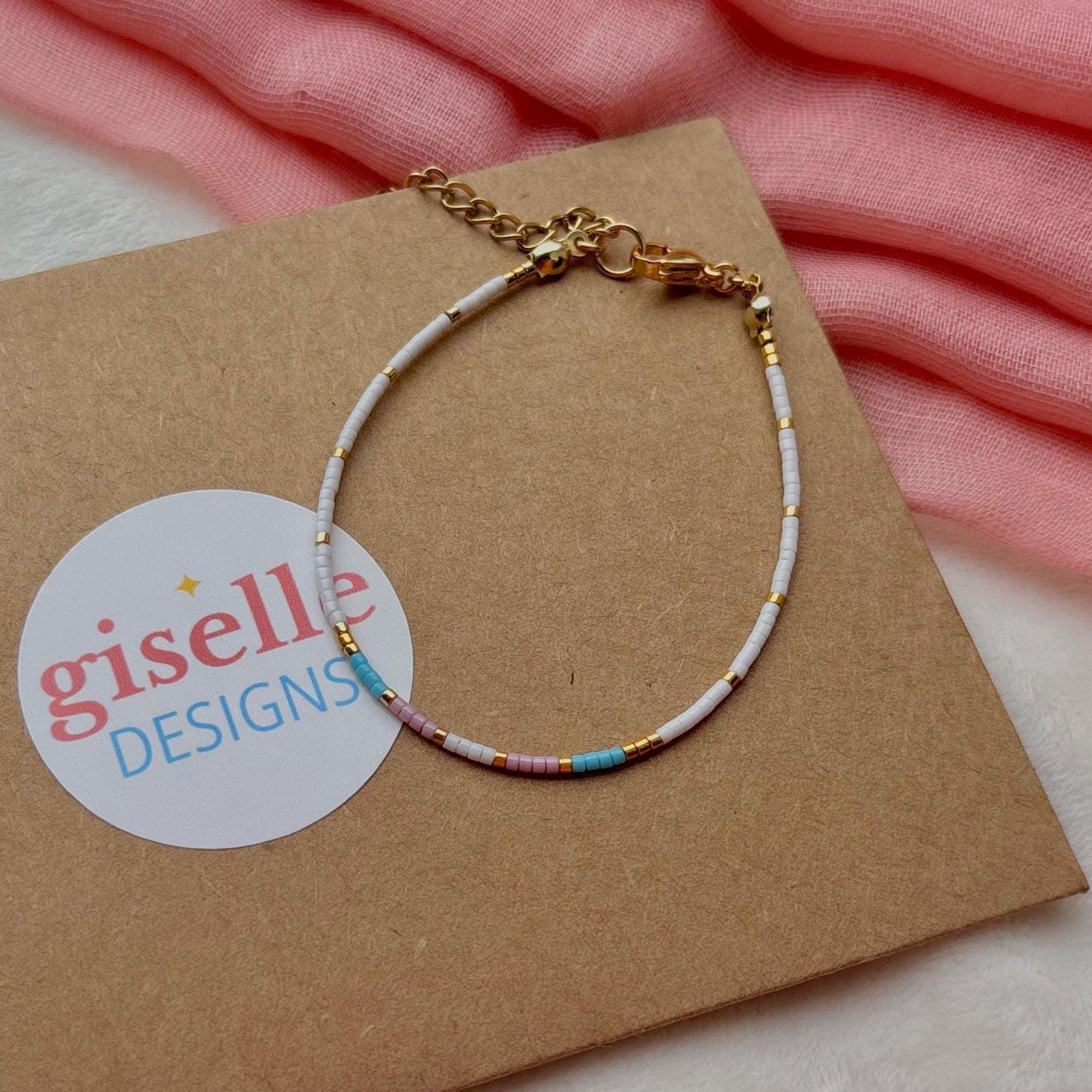 Trans bracelet on a brown card with 'giselle DESIGNS' logo, pink fabric in the background