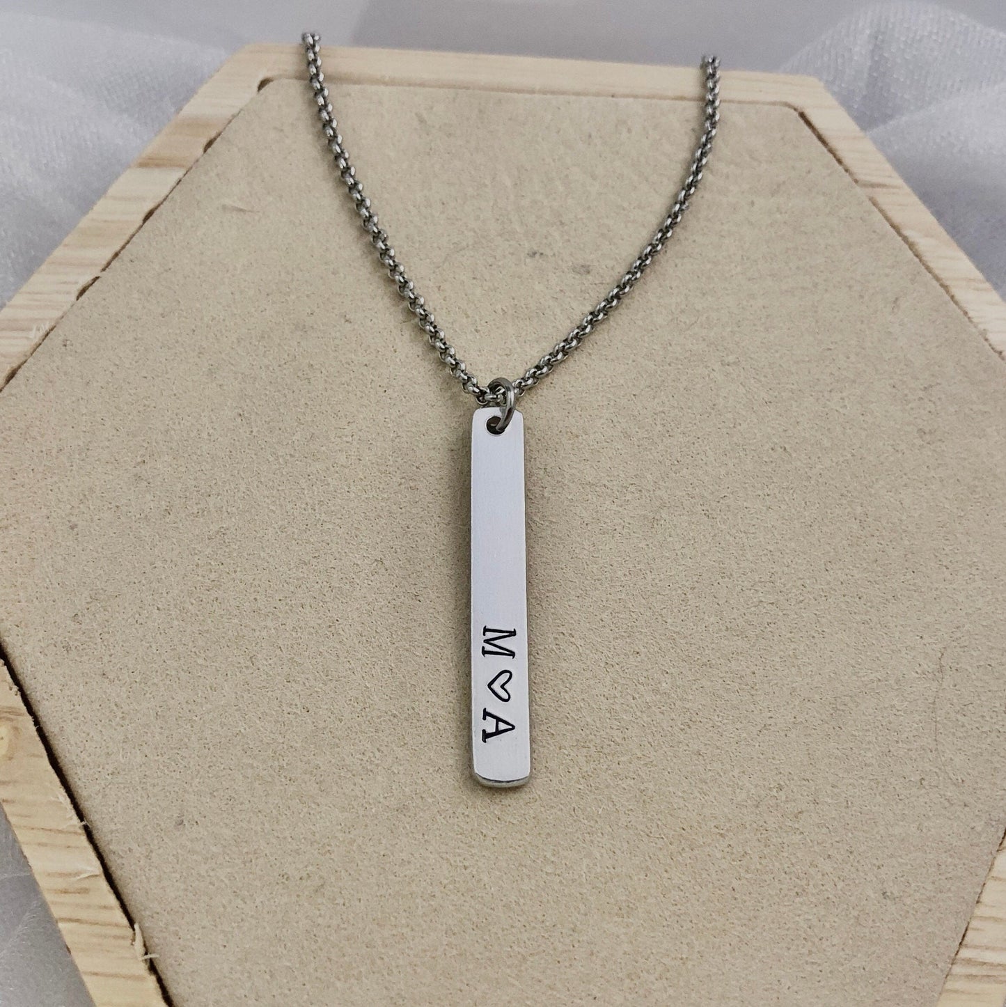 Necklace with a vertical bar pendant on a hexagonal wooden stand.