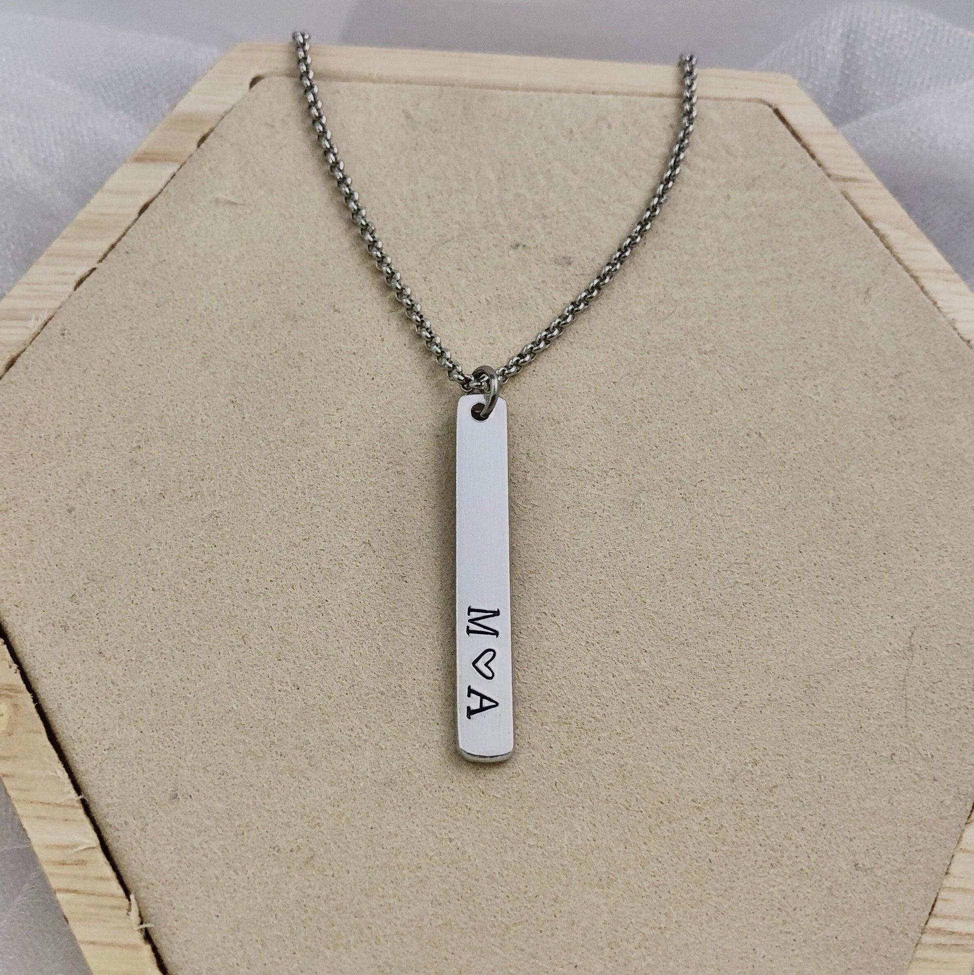 Necklace with a vertical bar pendant on a hexagonal wooden stand.