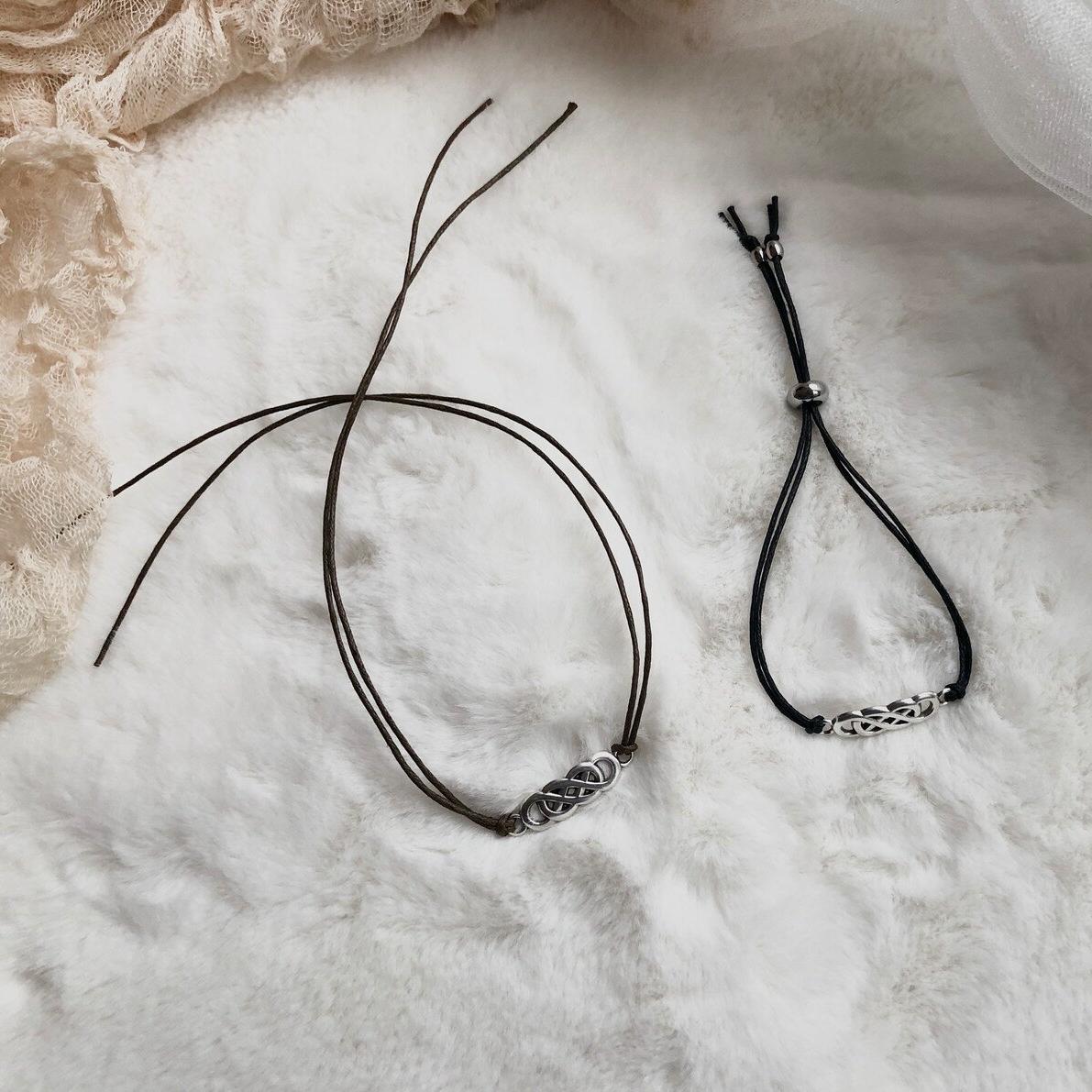 Two black cord necklaces with silver clasp on a textured white surface